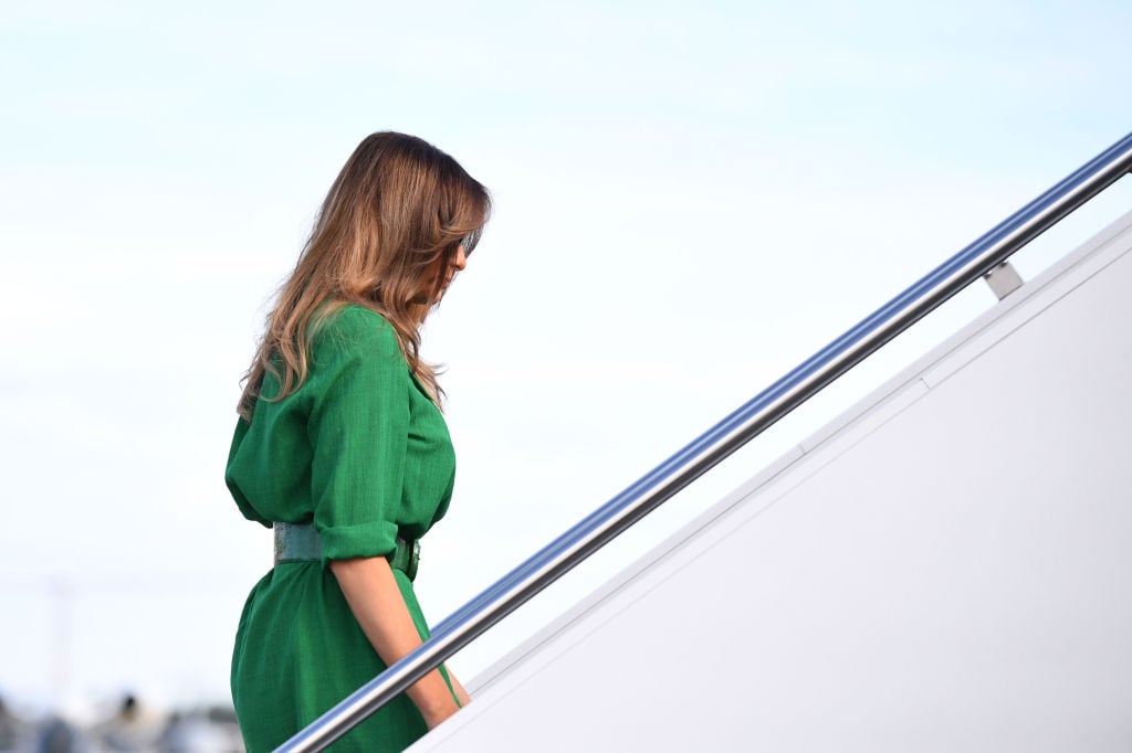 Melania Trump climbing up stairs in a green dress.