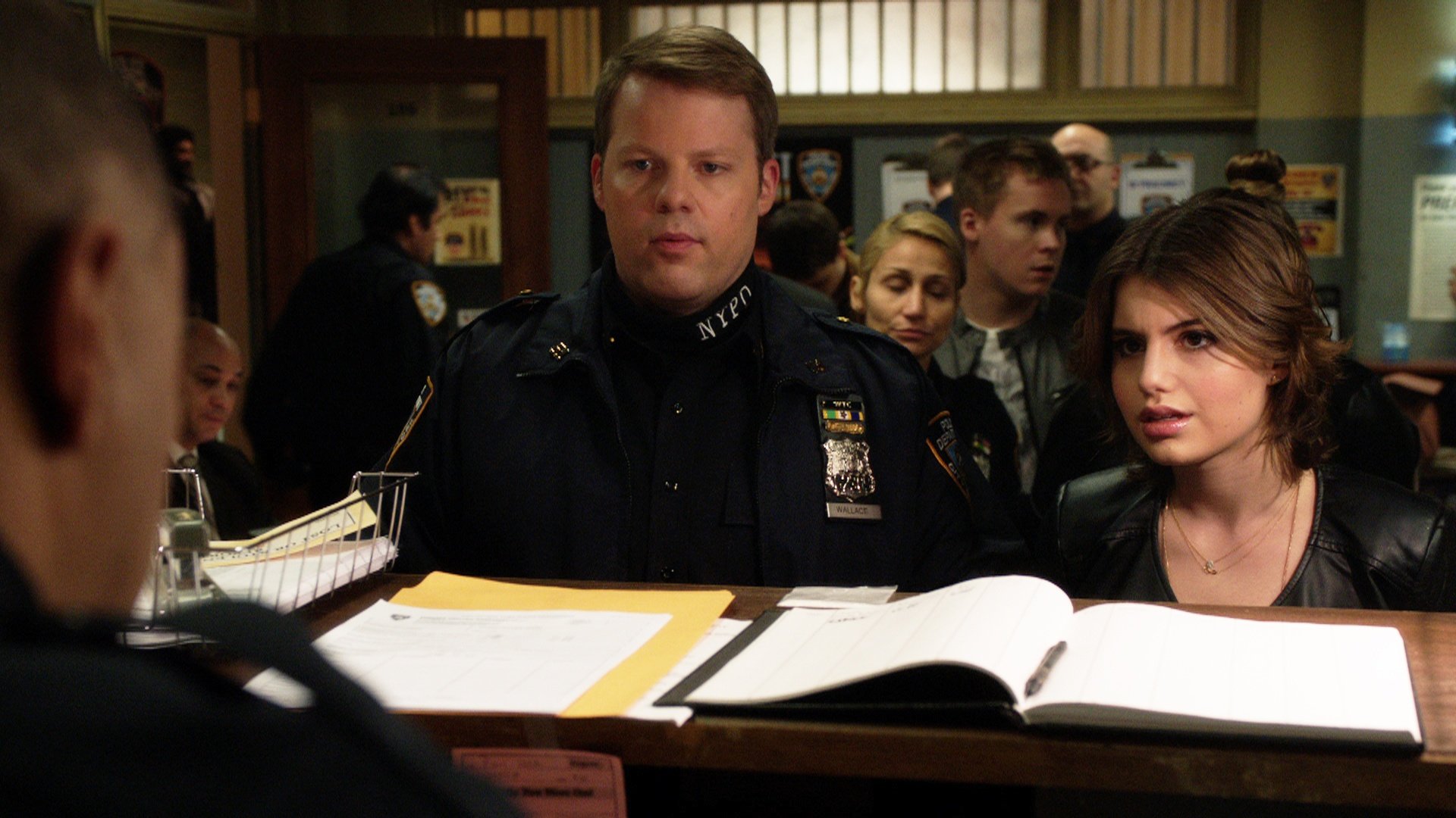 Sami Gayle as Nicky stands next to a police officer in a police station on Blue Bloods 