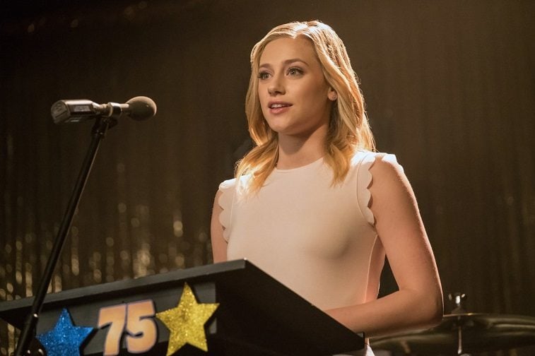 Lili Reinhart as Betty Cooper stands at a podium in front of a microphone in Riverdale