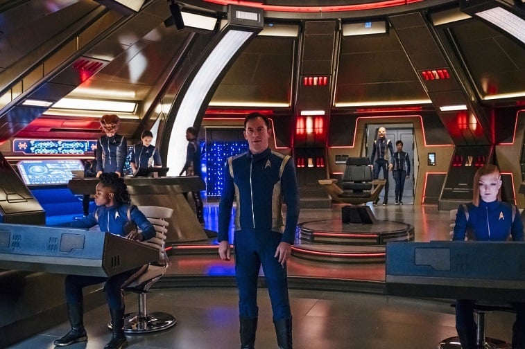A man stands on a craft surrounded while other people sit at screens beside him in Star Trek: Discovery