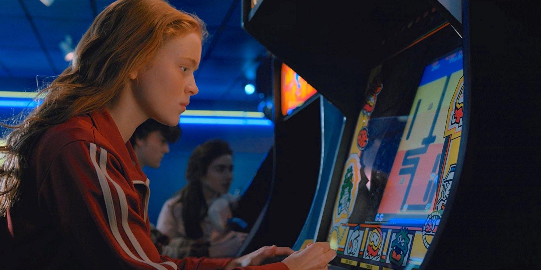 Sadie Sink as Max playing an old-fashioned video game machine in Stranger Things 2