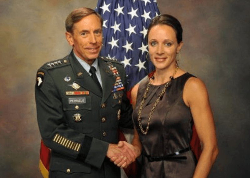 Paula Broadwell and David Petraeus posing for a photograph in front of a flag.