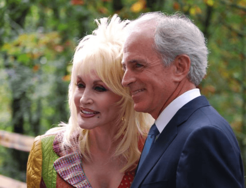 Dolly Parton and Carl Dean smile as they pose closely together.