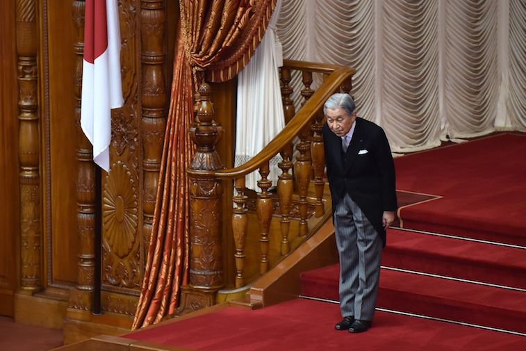 Japan's Emperor Akihito bows while standing on red stairs. Japan's Emperor Akihito bows while standing on red stairs.