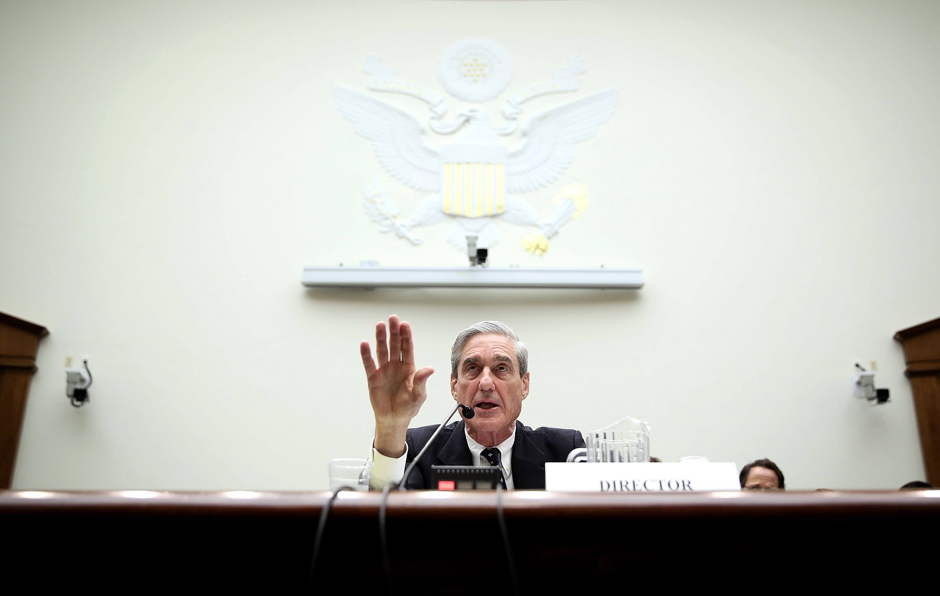Mueller sitting at a desk in front of large white wall.