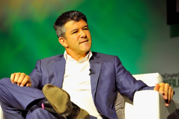 Travis Kalanick sitting down, wearing a blue suit with a white shirt while biting his bottom lip.