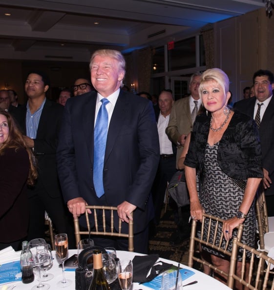 ivana and donald trump at a golf benefit standing behind gold chairs