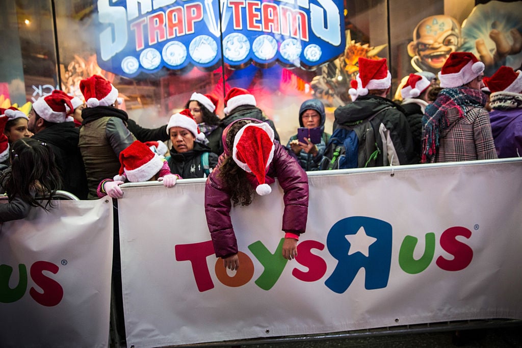 a kid in a santa hat draped over a toys r us sign in times square