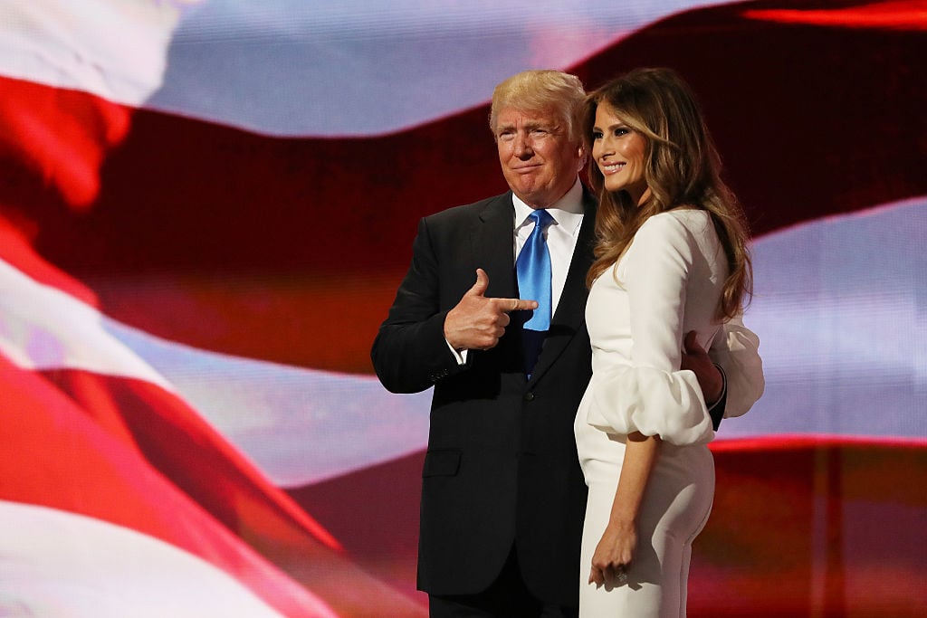 donald trump pointing to melania with an american flag behind them