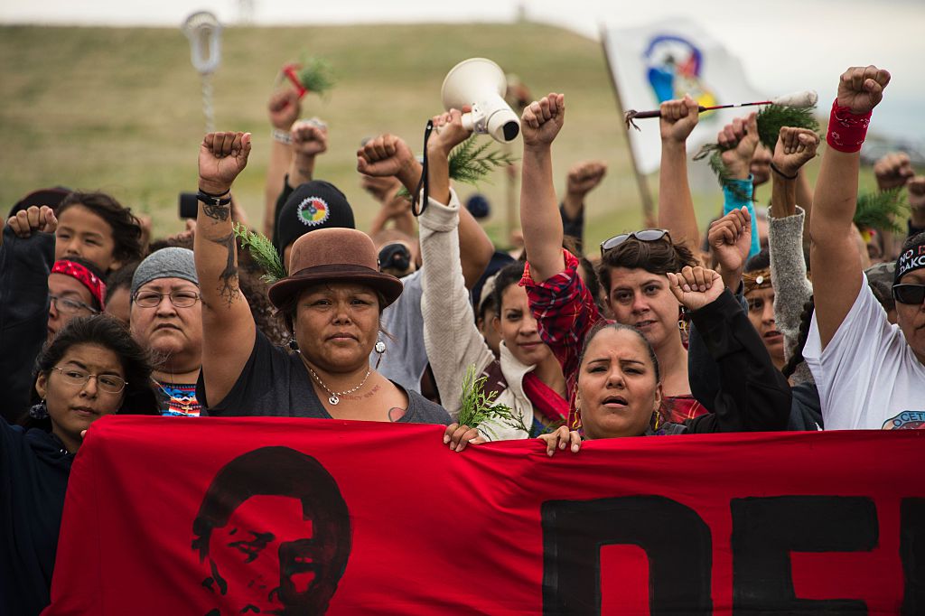 protesters at standing rock march together behind a red banner