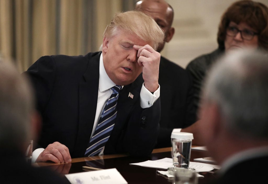 donald trump pinching his forehead in a dark suit and striped tie