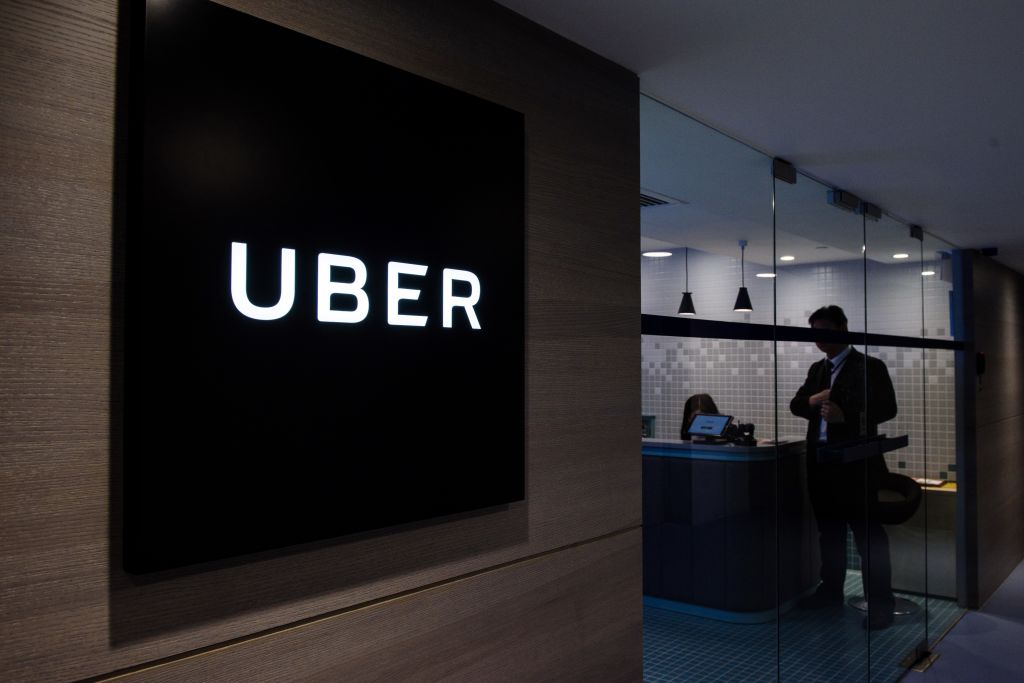 A display of the Uber logo in an office building with a shadowy figure in the background.