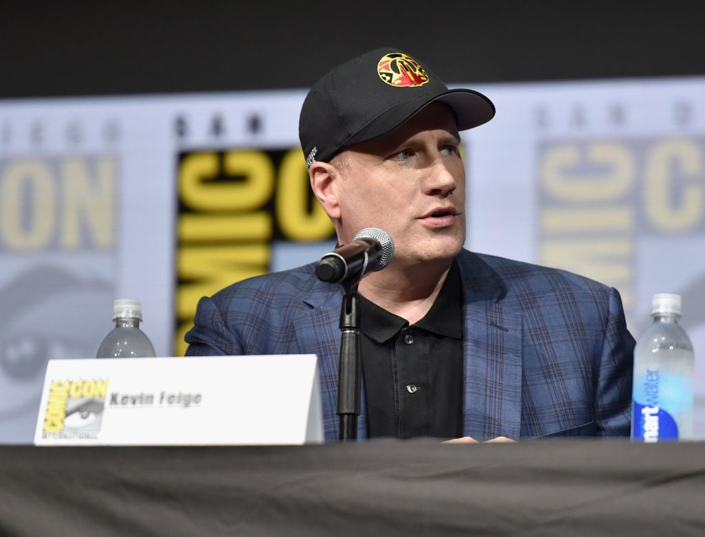 Kevin Feige in a cap and blue jacket speaking into a microphone at Comic-Con. Kevin Feige in a cap and blue jacket speaking into a microphone at Comic-Con.