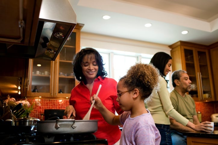 Grandmother cooking with granddaughter, rest of family talks in background