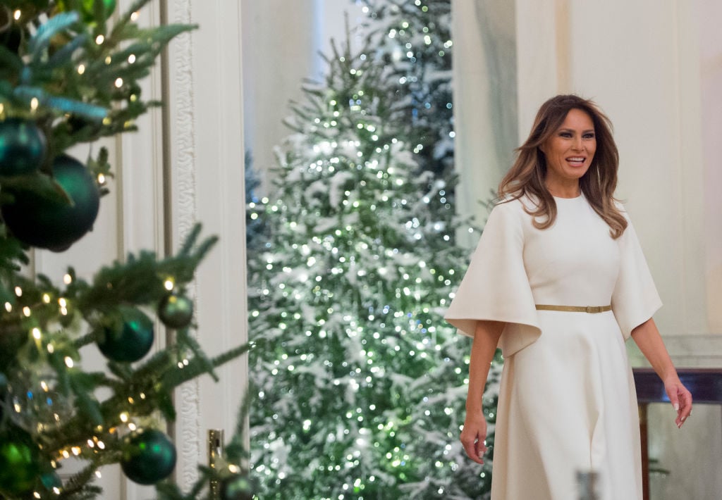 melania trump walks past a christmas tree