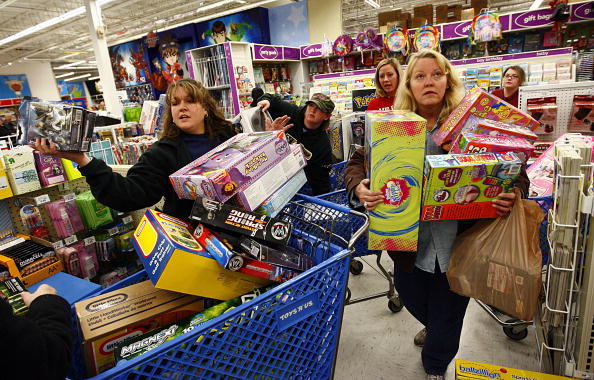 two women with loaded carts and their arms full wait in line during Black Friday