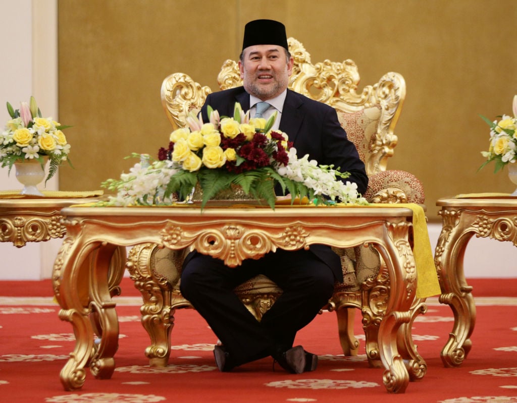 Sultan Muhammad V talks with Prince Charles while sitting in front of an elaborate gold throne. Sultan Muhammad V talks with Prince Charles while sitting in front of an elaborate gold throne.