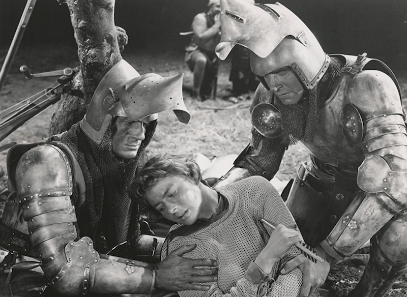 Joan being carried by two guards wearing armor. Joan being carried by two guards wearing armor.