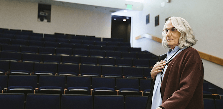 Maura stands in front of an empty lecture hall. Maura stands in front of an empty lecture hall.