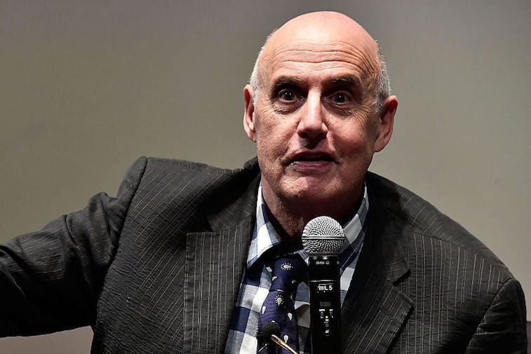 Jeffrey Tambor speaking in front of a microphone in a striped suit.