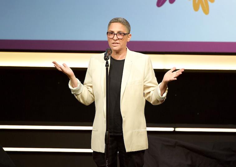 Jill Soloway stands in a yellow blazer while gesturing with her hands. 