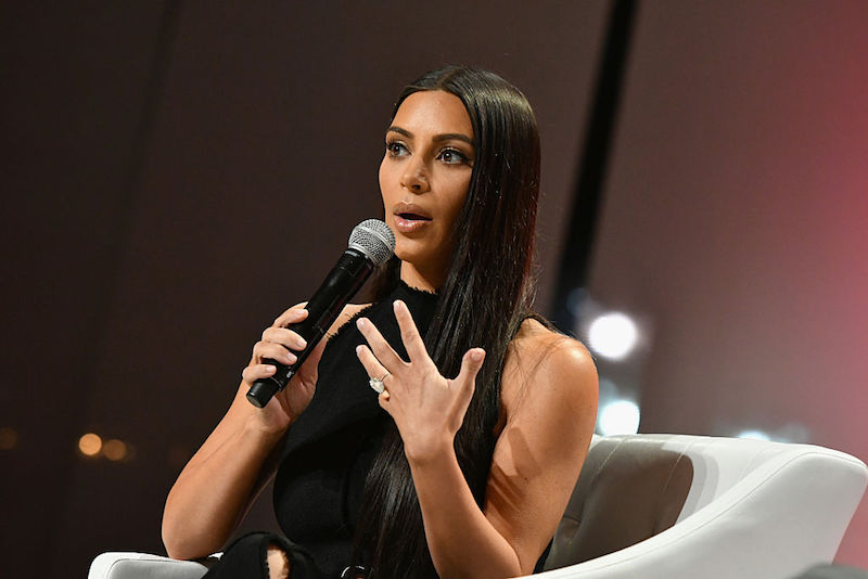 Kim Kardashian speaks into a microphone while sitting on a white chair on stage. Kim Kardashian speaks into a microphone while sitting on a white chair on stage.