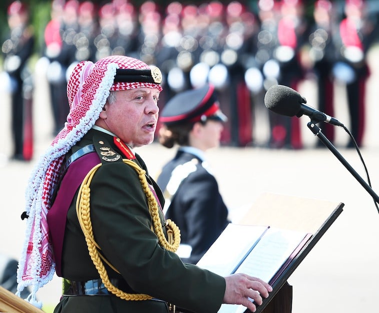King Abdullah II of Jordan stands in front of a podium while wearing a uniform. King Abdullah II of Jordan stands in front of a podium while wearing a uniform.