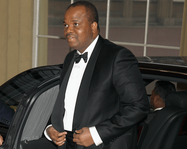 King Mswati III emerges from a black car wearing a tuxedo and tie.