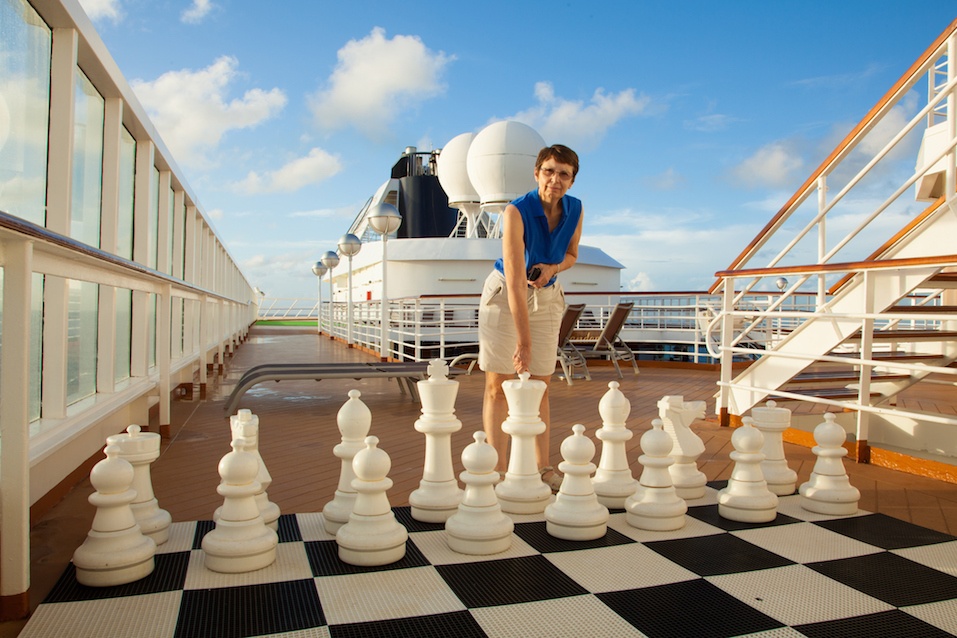 senior woman prepares to move a large chess piece on a cruise ship
