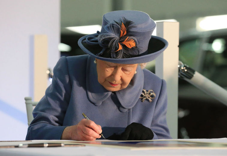 Queen Elizabeth signing papers on a desk. 