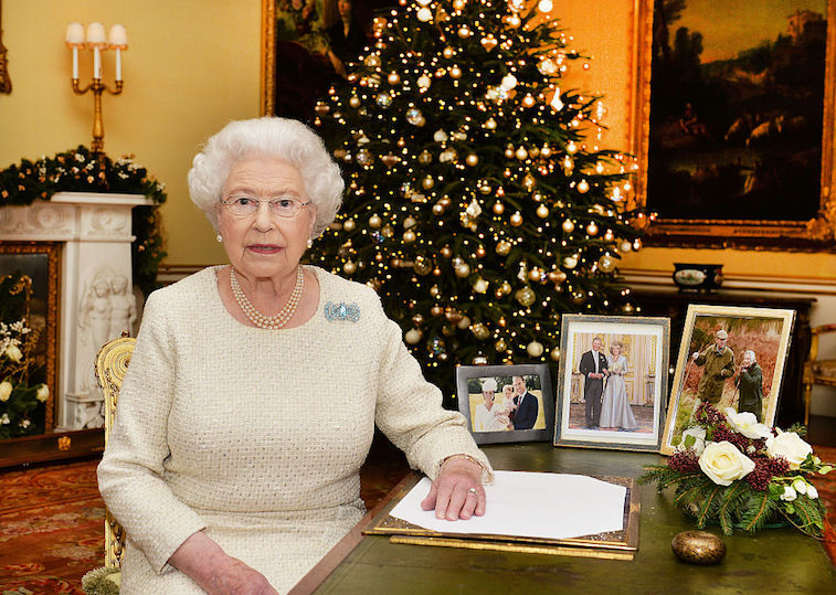 Queen Elizabeth sits at a desk surrounded by Christmas decorations. 