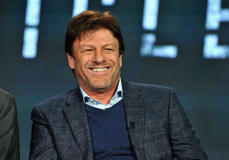 Sean Bean smiling while on a panel on stage.