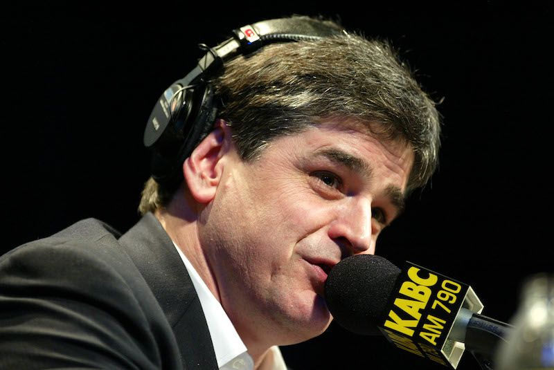 Sean Hannity speaking into a black microphone while wearing headsets. 