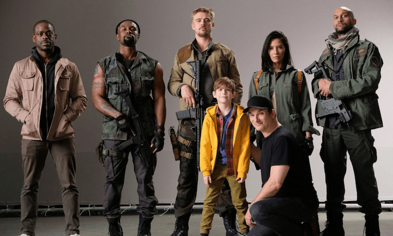 The cast of The Predator holding weapons and standing with a child.