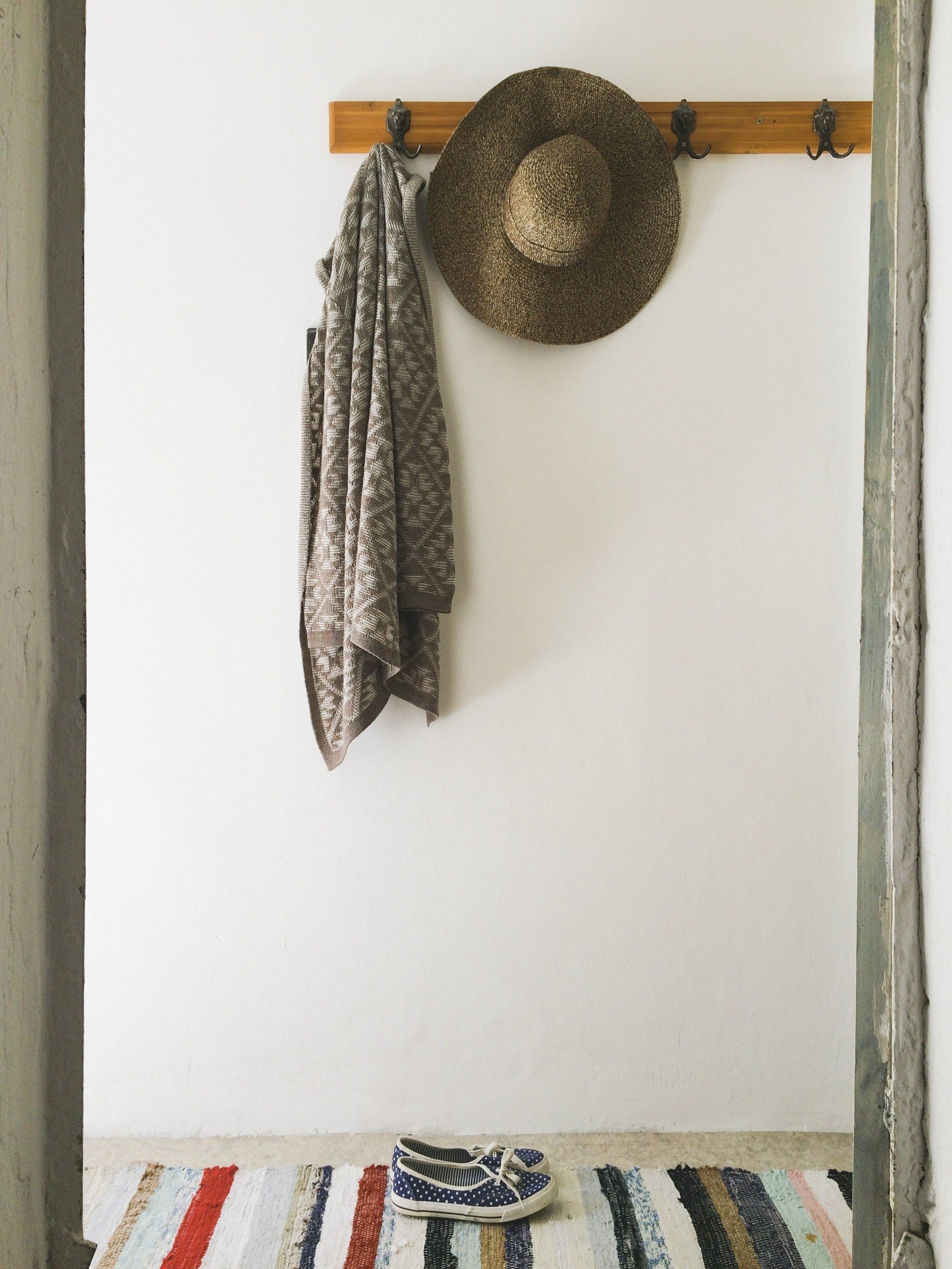 A coat and a hay cap hanging on the wall. Espadrilles underneath. Colorful rug.