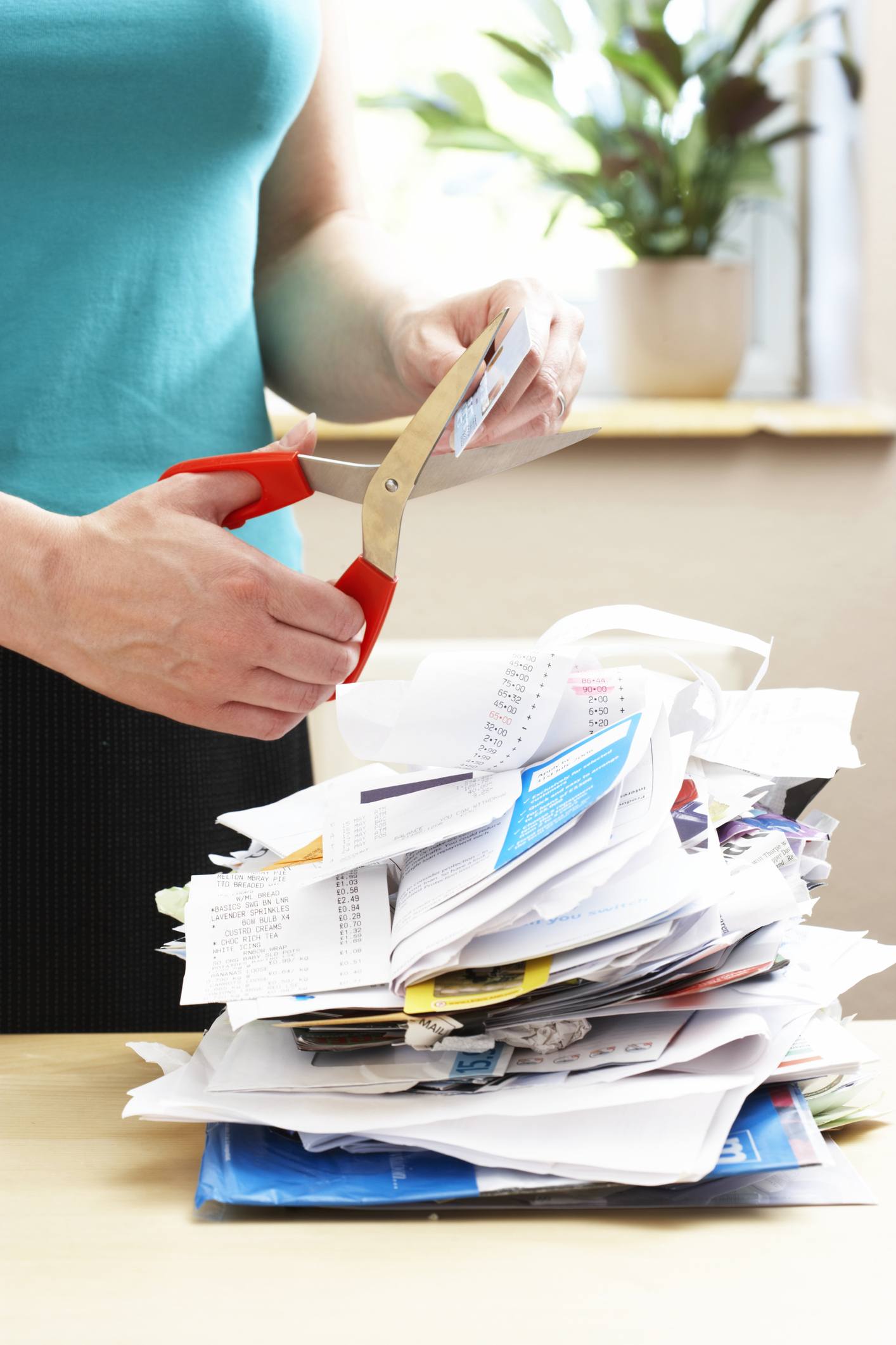 Woman cutting credit card over piled receipts and bills, close-up