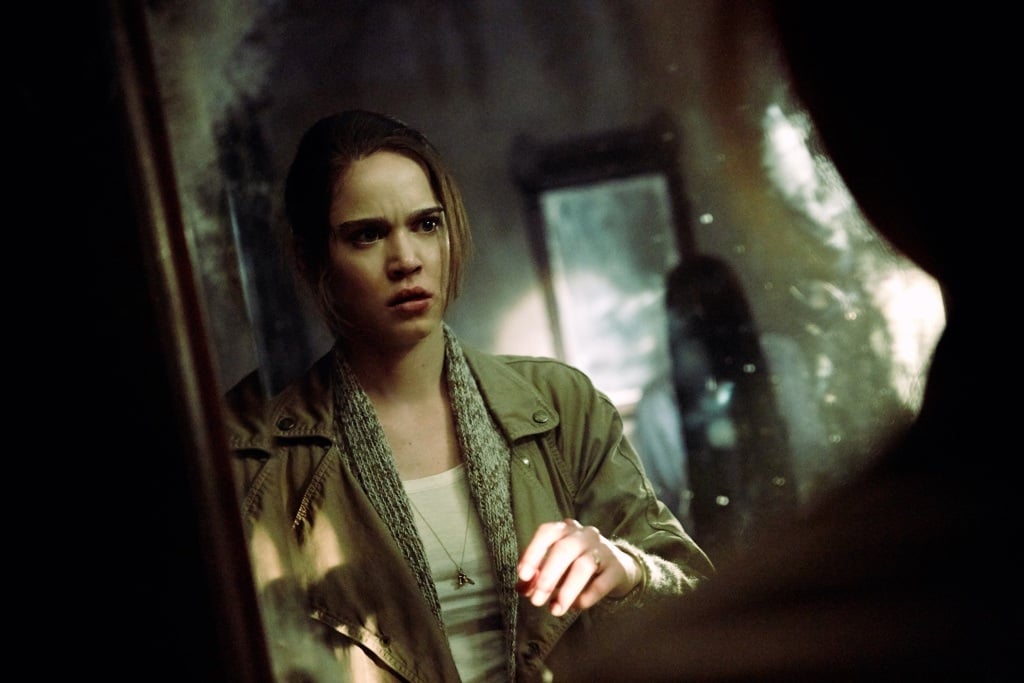 A woman looking at her reflection and a shadow behind her in the mirror. A woman looking at her reflection and a shadow behind her in the mirror.