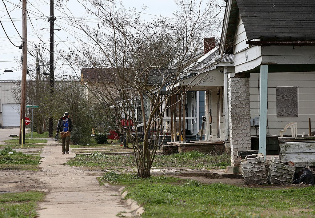 A pedestrian walks through a neighborhood with run down homes
