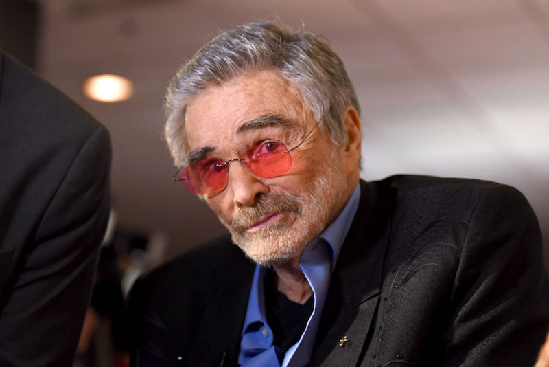 Burt Reynolds smiling while wearing a blue shirt and black jacket. Burt Reynolds smiling while wearing a blue shirt and black jacket.