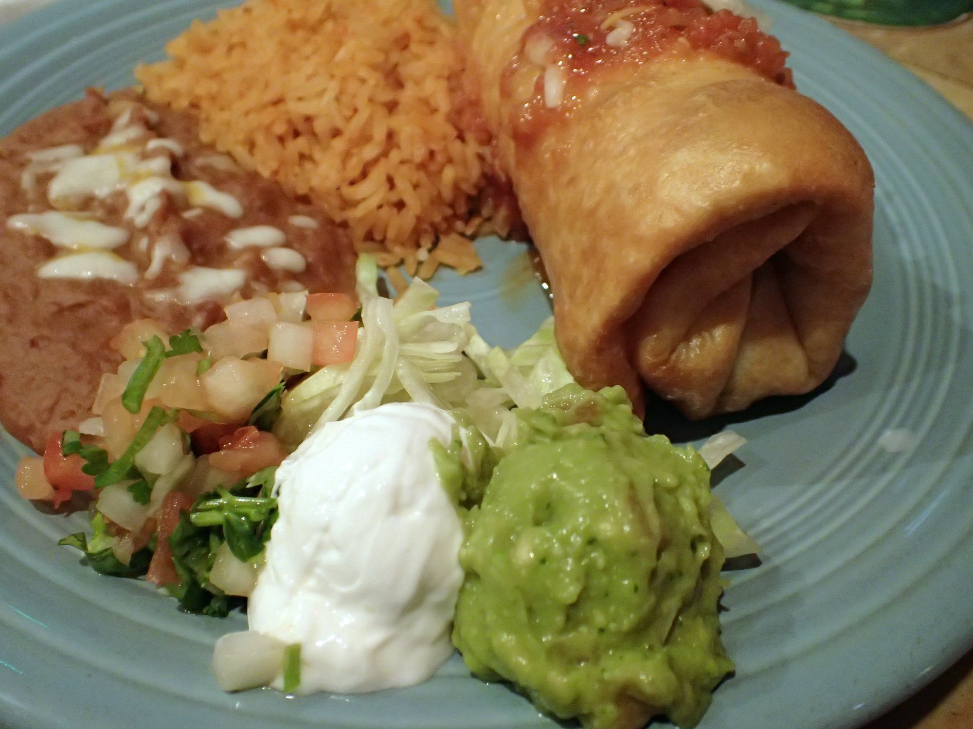 mexican chimichanga plate featuring spanish rice, refried beans, guacamole, pico de gallo, and sour cream on a blue plate