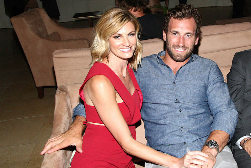 Erin Andrews and  Jarret Stoll sit on a sofa while holding hands. 