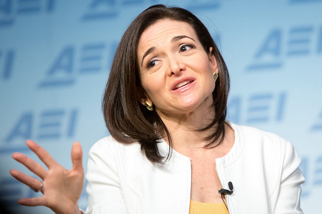 sheryl sandberg in a white blazer speaks against a blue background sheryl sandberg in a white blazer speaks against a blue background