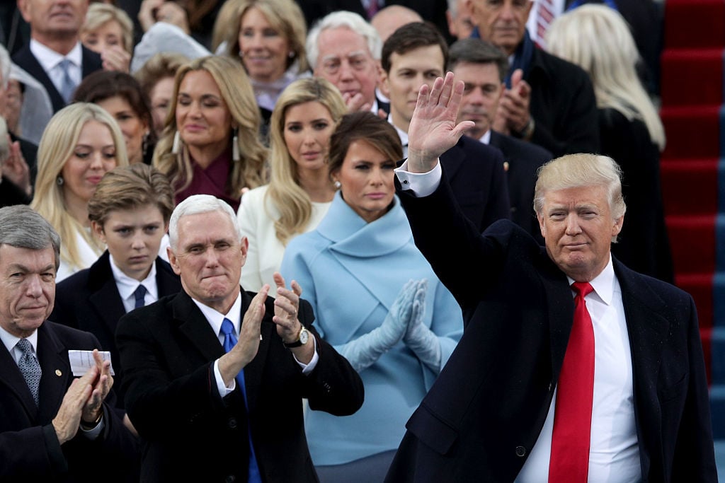 Melania Trump frowning and clapping standing behind Donald Trump as he waves.