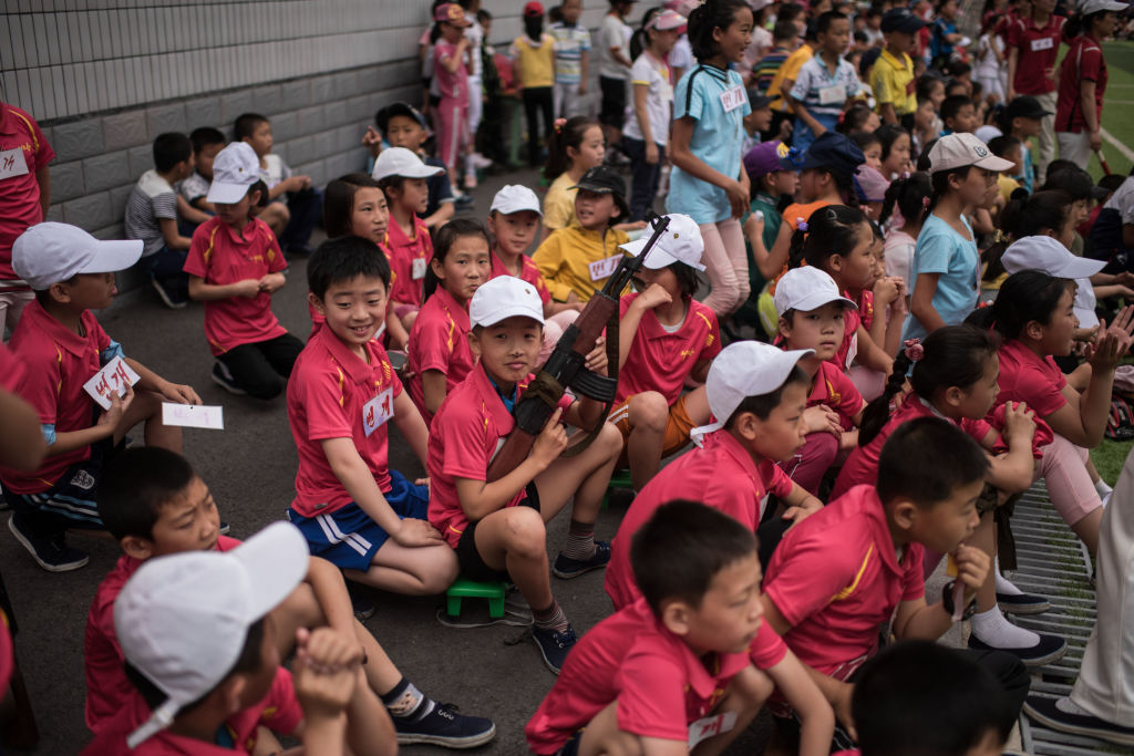 A boy holds a mock rifle as he sits with other children.