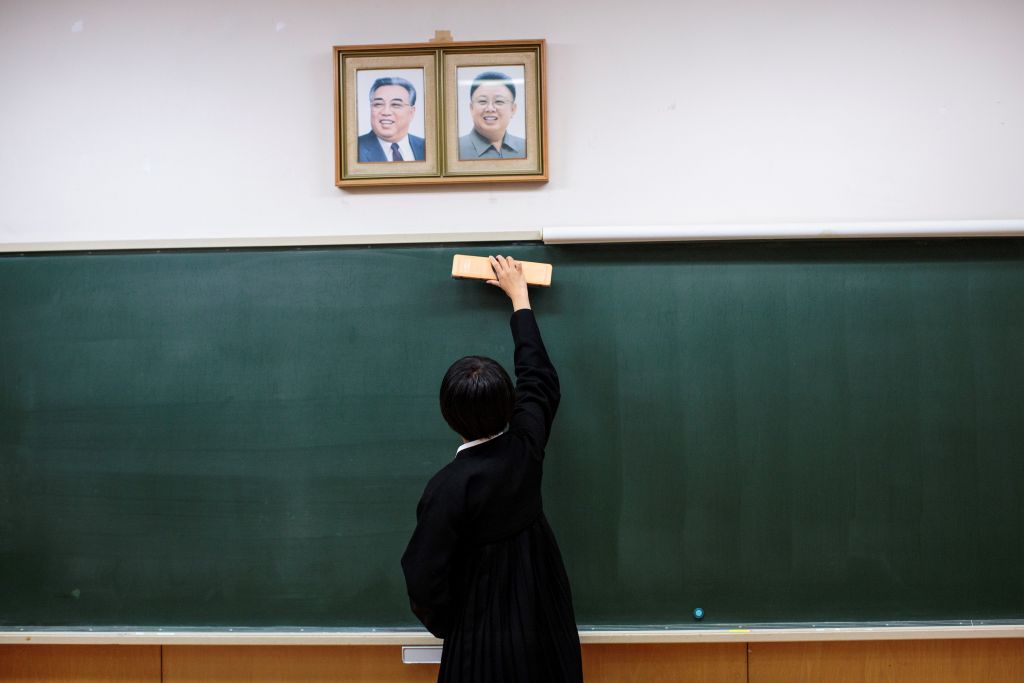 A student cleans the blackboard under portraits of late North Korean leaders Kim Il Sung and Kim Jong Il.