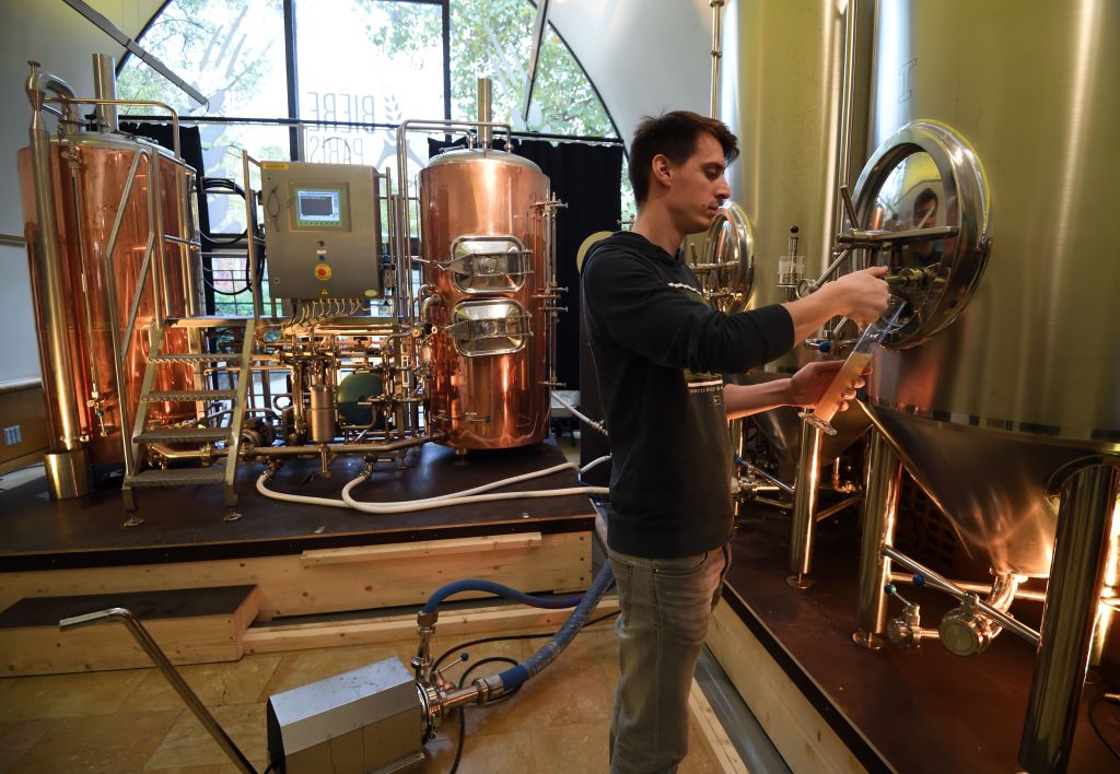 a brewer inspects a tank at a brewery in france, with copper stills behind him