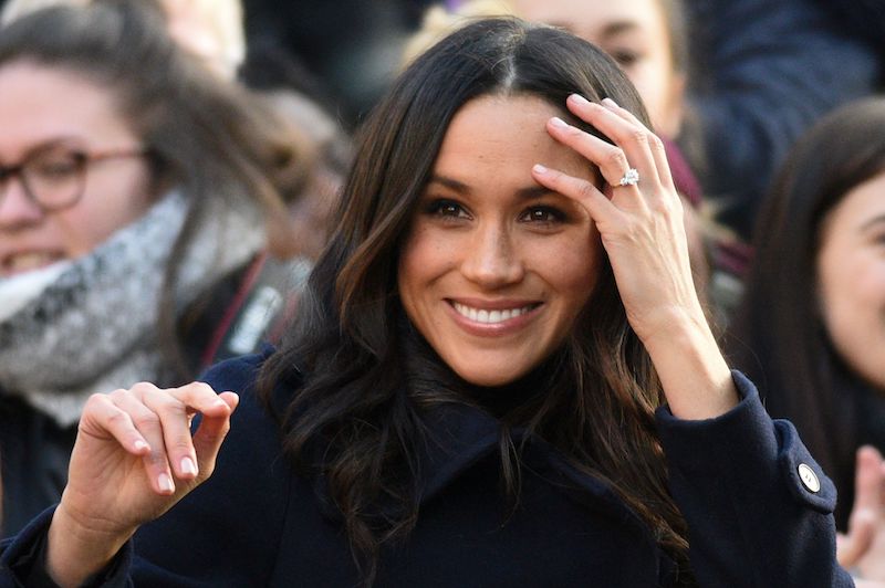 Meghan Markle smiles as she brushes her hair away from her face. 