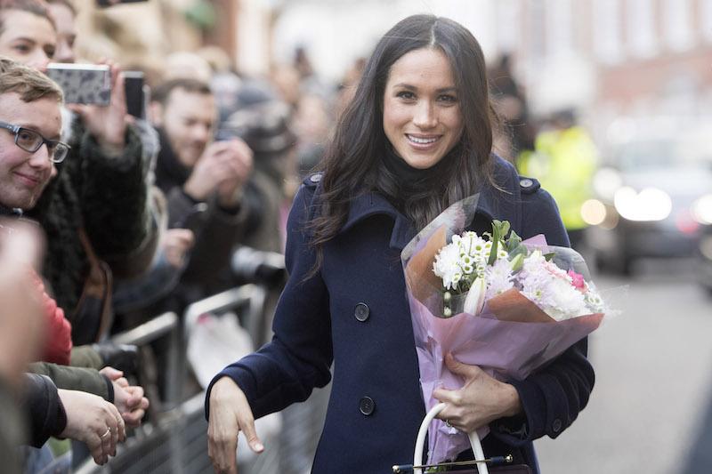 Meghan Markle smiling and holding a bouquet of flowers.