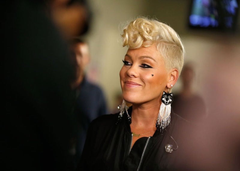 Pink smiling while wearing a black jacket and cat-themed earrings. Pink smiling while wearing a black jacket and cat-themed earrings.