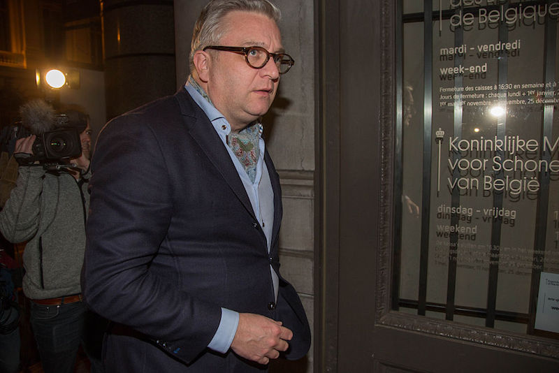 Prince Laurent stands in glasses wearing a blue suit. 